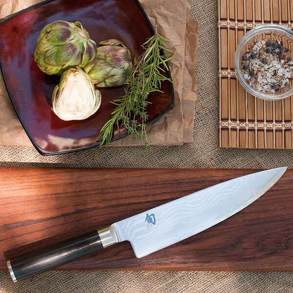 A Shun Classic Chef Knife on a wooden cutting board with artichokes and rosemary.