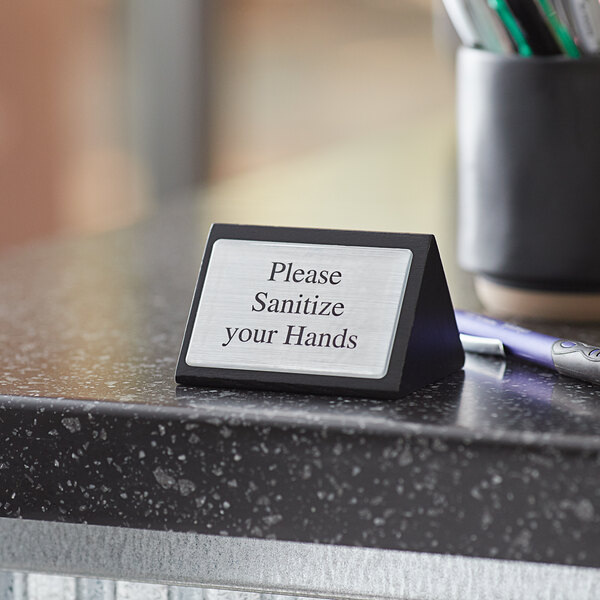 An American Metalcraft black wood double-sided sign with "Please Sanitize Your Hands" text on a counter.