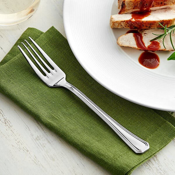 An Acopa Landsdale stainless steel fork on a napkin next to a plate of meat.