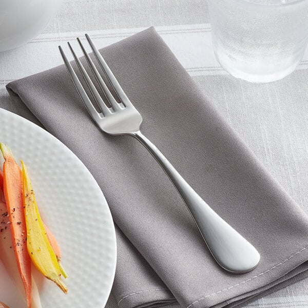 An Acopa Vernon stainless steel dinner fork on a napkin next to a plate of food.