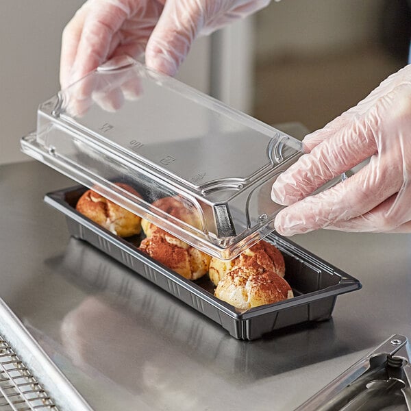 A gloved hand putting food in a Choice clear rectangular food container.