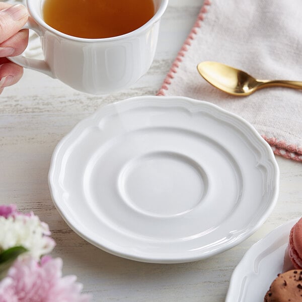 A hand holding a cup of tea with a saucer on a plate.