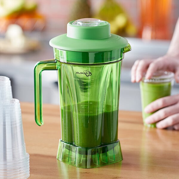 A person using an AvaMix green plastic blender to make green juice.