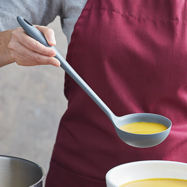 A woman using a Tablecraft gray flexible silicone ladle to serve soup.