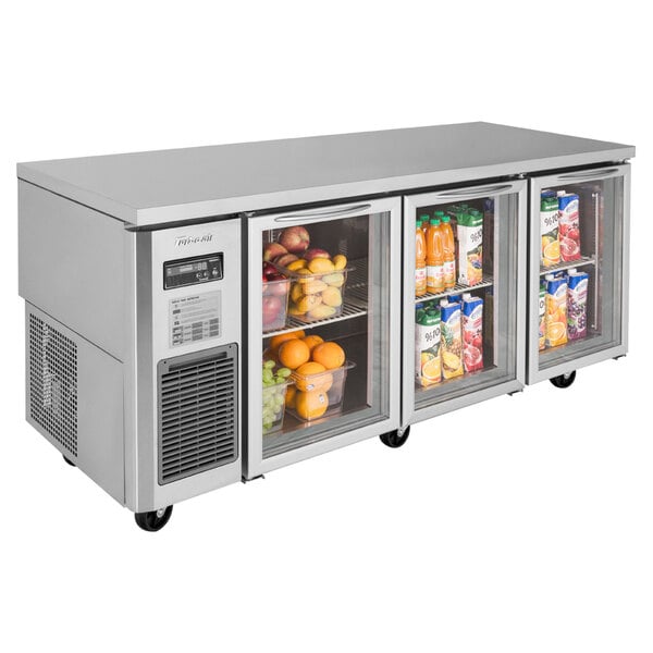 A Turbo Air undercounter refrigerator with three glass doors holding fruit and juice.