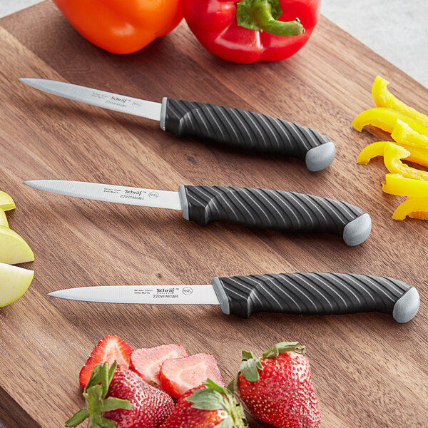 A Schraf 3-pack of paring knives with black and silver knives on a wood cutting board.