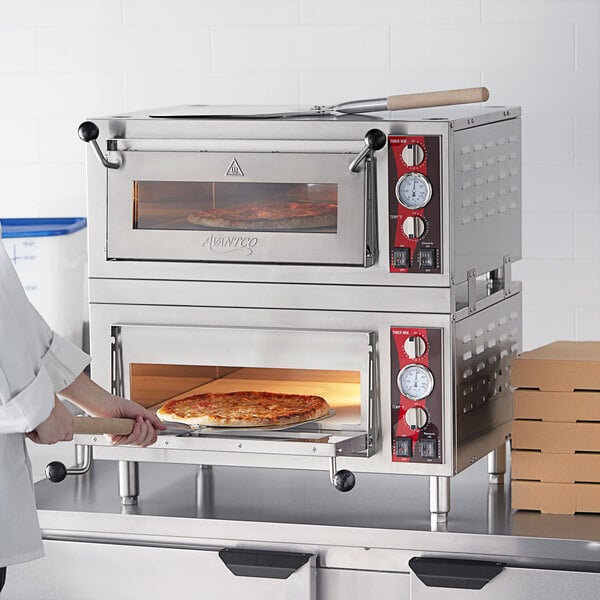 A woman putting pizza in an Avantco countertop pizza oven.