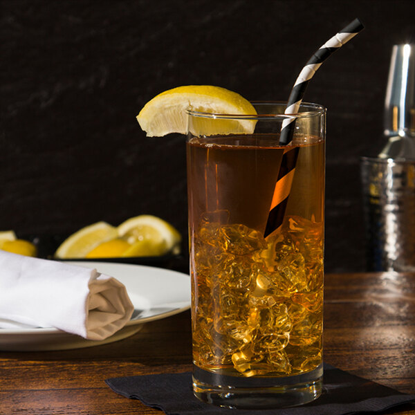 A black and white eco-flex paper straw in a glass of iced tea with a lemon slice and ice cubes.