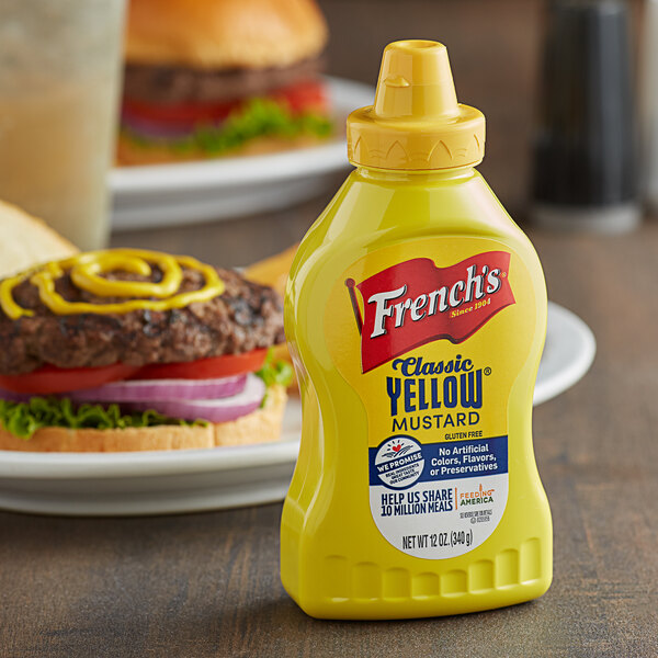 A close up of a yellow bottle of French's Classic Yellow Mustard next to a burger.