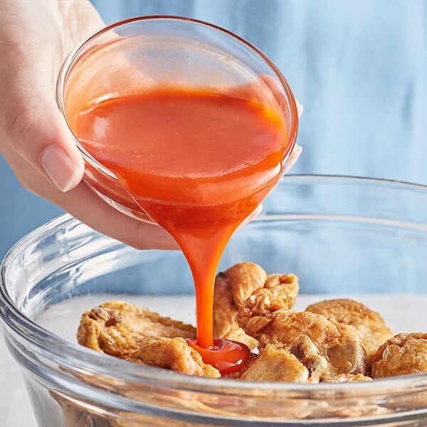 A person pouring Frank's RedHot XTRA Hot Buffalo Wings Sauce into a bowl of chicken wings.