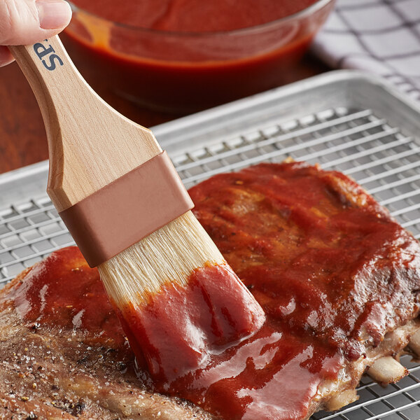 A person using a brush to apply Cattlemen's Louisiana Hot and Spicy BBQ Sauce to a piece of meat.