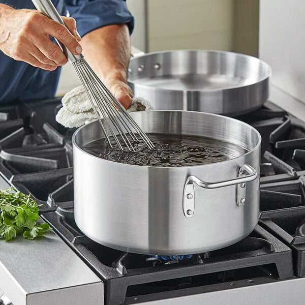 A person stirring liquid in a Choice aluminum sauce pot on a stove.