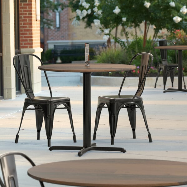 A Lancaster Table & Seating Excalibur round dining table with a textured wood finish and cross base plate on an outdoor patio.