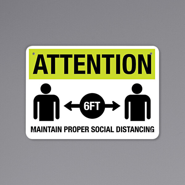 A black and yellow rectangular sign with text that reads "Attention - Maintain Proper Social Distancing" and includes a symbol.