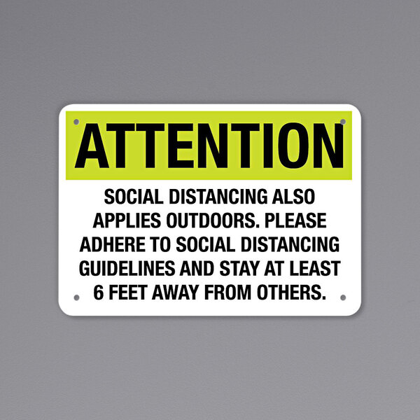 A black and yellow aluminum sign that says "Attention / Social Distancing"