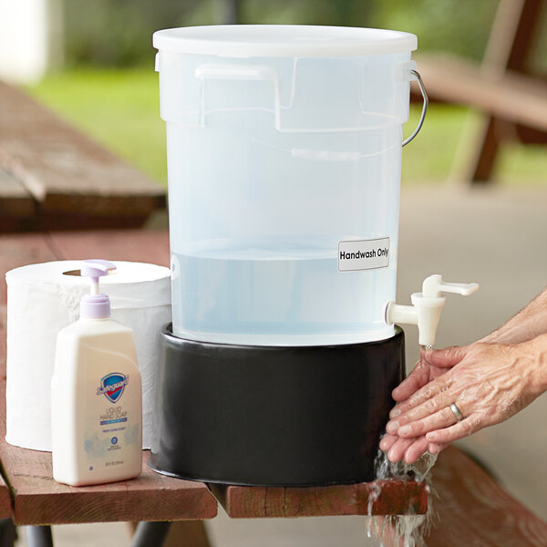 A person pouring water into a clear round beverage dispenser with a black base.