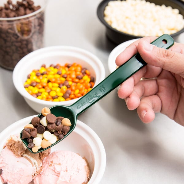 A hand using a Carlisle forest green salad bar spoon to add chocolate chips to a bowl of ice cream.