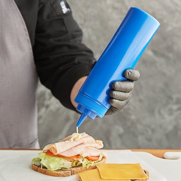 A hand in a glove squeezing blue sauce onto a sandwich.