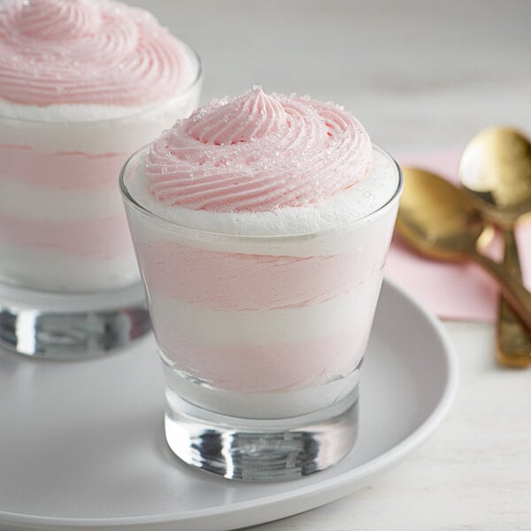 Two glasses of pink and white Knorr Neutral Mousse dessert on a plate with gold spoons.
