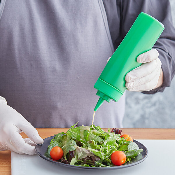 A person wearing gloves and holding a Choice green squeeze bottle of sauce over a plate of salad.