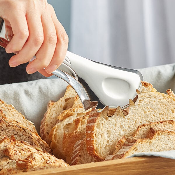 A hand using Acopa stainless steel bread tongs to pick up a slice of bread.