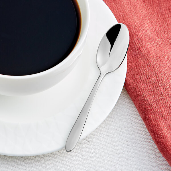 An Acopa Remy stainless steel demitasse spoon on a plate with a cup of coffee.
