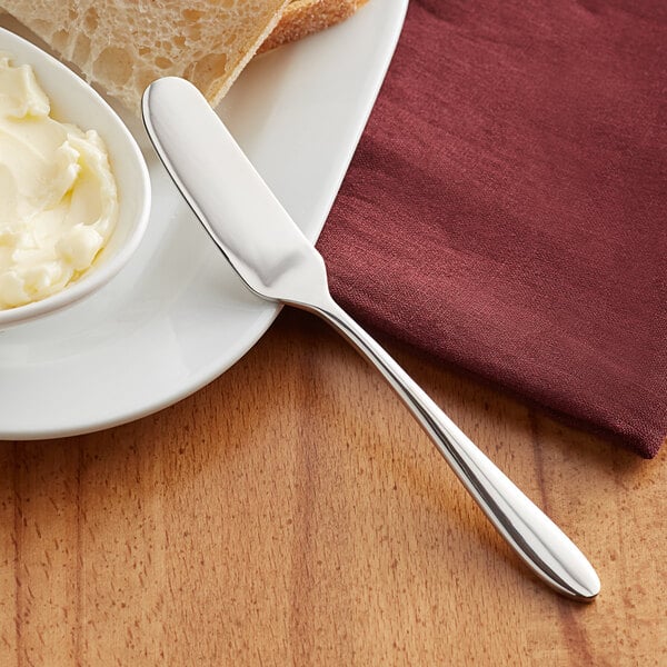 An Acopa Remy stainless steel butter knife on a plate with bread and butter.