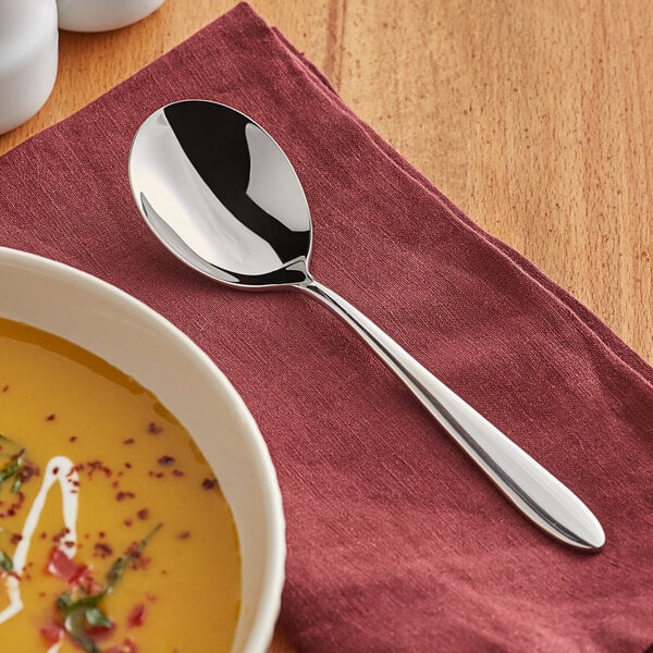 An Acopa Remy stainless steel bouillon spoon in a bowl of soup.