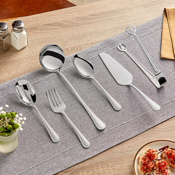 A table set with Acopa stainless steel serving utensils including spoons, forks, and a knife.