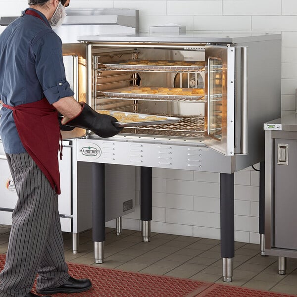 A man wearing an apron and oven mitts putting food into a Main Street Equipment convection oven.