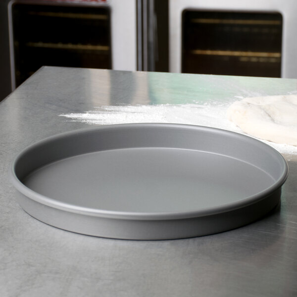 An American Metalcraft hard coat anodized aluminum pizza pan on a white countertop with white flour.