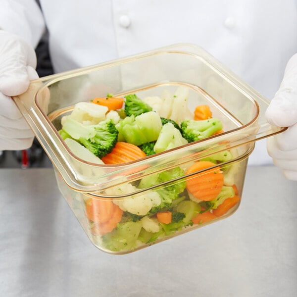 A person in gloves holding a Carlisle amber plastic food pan of vegetables.