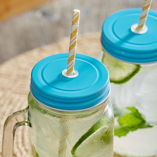 Two Acopa rustic light blue metal mason jar lids with straw holes on two glasses filled with drinks.