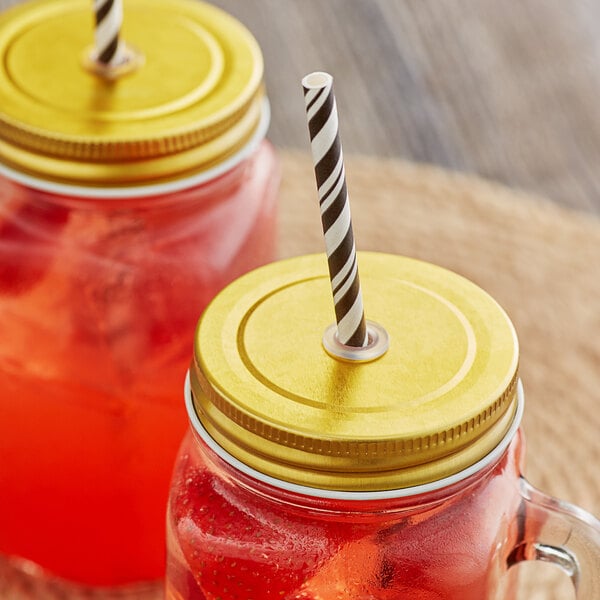 Two Acopa Rustic Charm gold metal drinking jar lids with straws on mason jars on a table.