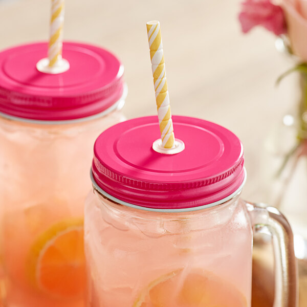 Two Acopa Rustic Charm mason jars with pink lids and straws filled with pink lemonade.