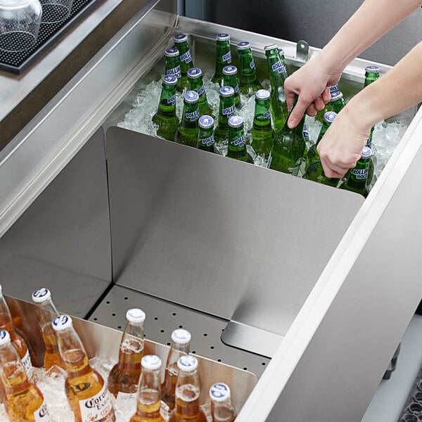 A person placing stainless steel beer box dividers in a cooler with glass bottles of beer.