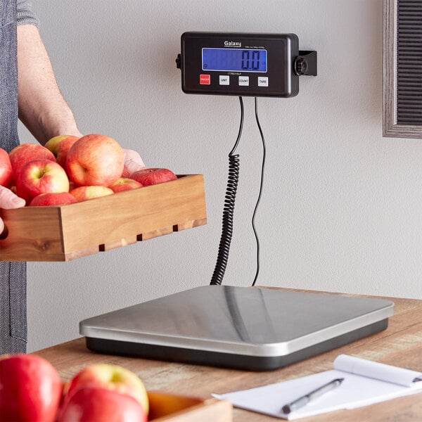 A person using a Galaxy low-profile digital receiving scale to weigh a box of apples.