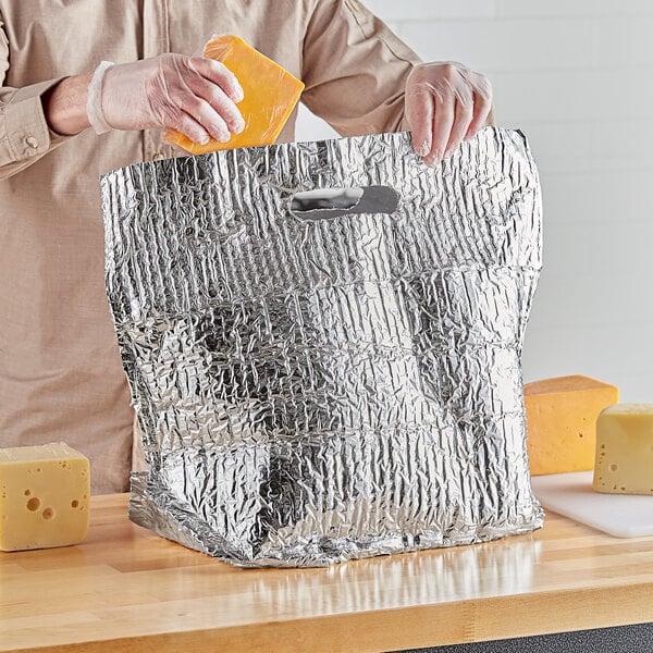 A person in a plastic glove putting cheese into a Lavex insulated delivery bag.
