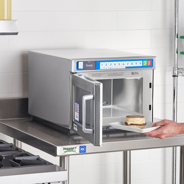 A hand placing a plate of food in a Solwave commercial microwave.