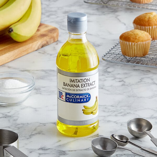 A bottle of McCormick Culinary Imitation Banana Extract on a counter next to a bunch of bananas.