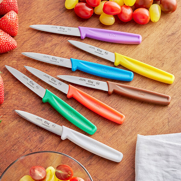 A group of Choice paring knives with different colored handles on a table with fruit.