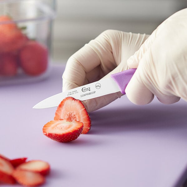 A person in gloves uses a Choice smooth edge paring knife with a purple handle to cut a strawberry.
