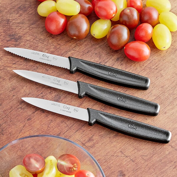 Choice paring knife set with black handles on a table with tomatoes and grapes.