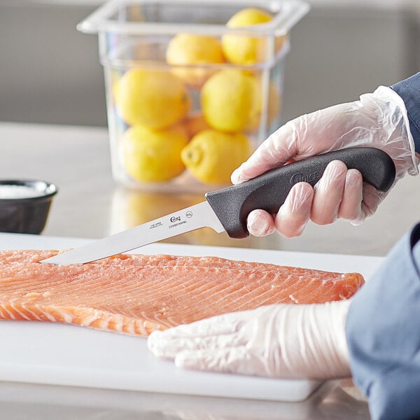A person using a Choice narrow stiff boning knife to cut a piece of fish.