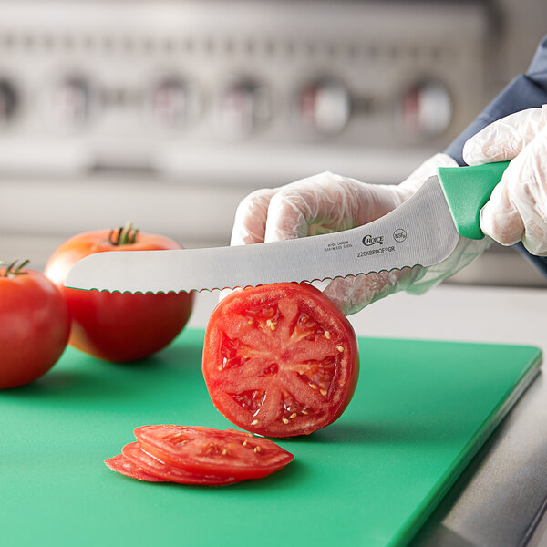 A person using a Choice bread knife with a green handle to cut a tomato.