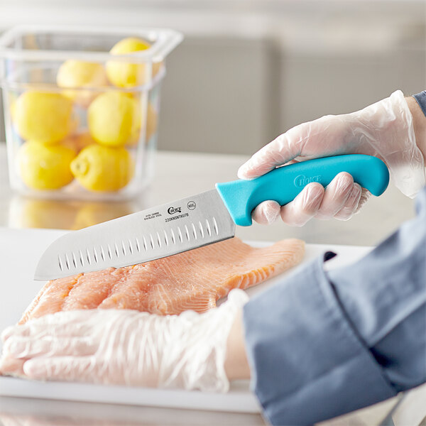 A person holding a Choice Santoku Knife with a neon blue handle cutting a piece of meat.