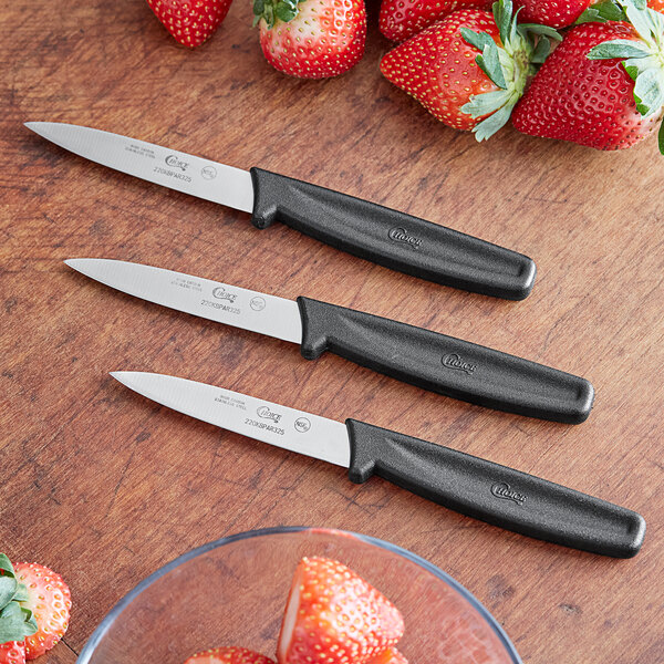 Three Choice 3 1/4" Smooth Edge Paring Knives with black handles next to strawberries.