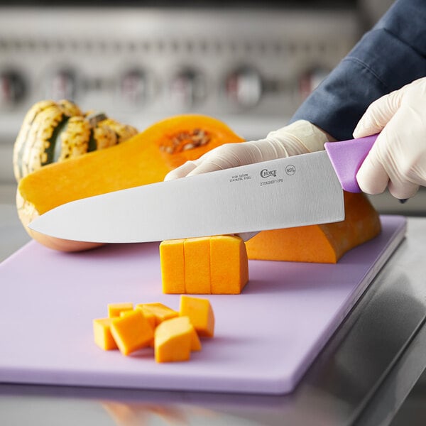 A person uses a Choice 10" chef knife with a purple handle to cut up a pumpkin.