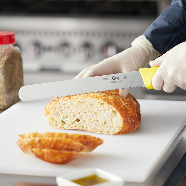 A person using a Choice yellow serrated bread knife to slice bread.