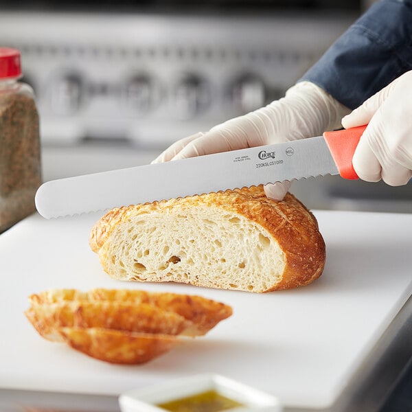 A person using a Choice red serrated bread knife to slice bread.